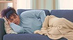 Woman suffering from PMS pain while laying on a sofa at home. Young female with chronic endometriosis covering herself with a blanket on a couch. Lady feeling unwell, in early stages of a miscarriage