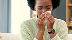 Sick woman blowing her nose with a tissue in a warm sweater. Face of an ill african woman with cold or flu wiping snot and looking tired, sitting alone at home in the living room