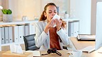 Sick business woman sneezing and blowing her runny nose with a tissue while working in an office. Female feeling unwell with flu, cold and covid symptoms. Congested with sinuses and spring allergies