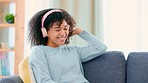 Young carefree woman listening to music on her phone while sitting on a sofa in her living room at home. Happy female dancing and smiling while streaming songs from a playlist app over the weekend