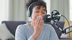 Cheerful woman recording a podcast while wearing headphones and talking over a microphone for her blog. Funny African blogger using audio equipment and doing a live radio broadcast from home