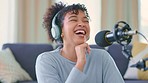 Cheerful woman recording a podcast while wearing headphones and talking over a microphone for her talk show. Funny African blogger using audio equipment and doing a live radio broadcast from home