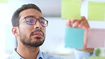 Young business man brainstorming and planning a marketing strategy alone in an office at work. Happy male corporate professional smiling while writing down ideas and doing research for his company