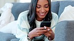Young woman texting on her phone while relaxing on the couch at home. Cheerful woman flirting online while using social media app or browsing the internet for some entertainment over the weekend