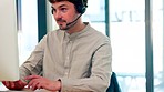 Male call center agent with a headset working on desktop computer in an office. A virtual assistant or sales representative using live chat communication app for an online customer support service