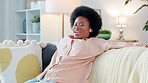Woman listening to music with wireless earphones while relaxing on the couch alone at home. One young, happy and cheerful black female dancing, singing, and enjoying her favorite songs on the sofa