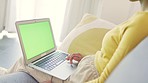 Woman scrolling and browsing online on a laptop with a green screen while relaxing on the couch at home. One person using social media or watching movies on the internet while sitting on the sofa