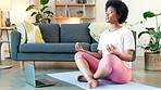 Young black woman meditating with a laptop in the lounge at home. One serious and relaxed female sitting in the lotus position and doing a daily yoga routine in the living room alone for relaxation
