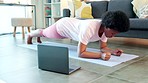 Woman exercising at home for health and core strength, inside on a sunny morning. Casual young female following an online fitness tutorial on her laptop, holding planking position on a yoga mat