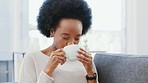 Young African woman feeling refreshed and happy while enjoying a cup of coffee or tea on the couch at home. Female with afro looking carefree and content while enjoying her free time over the weekend