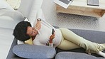 Top view of a woman using a phone to browse online and chat with friends on social media while relaxing on the couch alone at home. One black female searching the internet and texting on the sofa