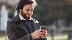 Handsome business man using a phone outside on a cold morning. Attractive male looking happy and excited, texting while standing alone in an urban park. Trendy young professional guy checking emails