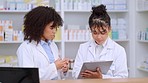 Two female pharmacists using a tablet and discussing work in pharmacy. Professional young chemists talking about prescription or chronic medication, taking notes and working in a clinic or dispensary