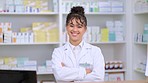Portrait of a pharmacist with folded arms against a background of prescription medication. Happy young professional health care worker waiting to diagnose and prescribe pills at a clinic dispensary