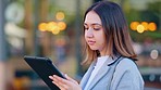 A young female journalist writing a story on a tablet outdoors on a street of a city. A young and stylish woman news reporter typing a blog about a recent story in an urban town