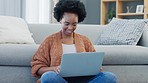 African woman typing on her laptop to send an email while sitting at home. Happy female with afro searching the internet, streaming movies or doing online shopping from the comfort of her home. 