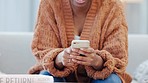 Woman sending a text message, browsing social media or surfing the internet on her phone while sitting in the living room at home. Closeup of the hands of a black female holding wireless technology
