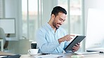 Happy accountant browsing the internet on a tablet and sitting in an office. Male financial advisor laughing at social media clickbait from his workplace. Stock broker smiling at funny internet posts