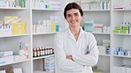 Friendly pharmacist laughing while standing in front of shelves of medicine, ready to advise patients or sell medication. Happy, caucasian female doctor working at a pharmacy of a hospital or clinic.