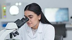 Clinical Laboratory Technician using microscope to analyze medical test samples in a lab. Young female Indian Medical lab scientist looking at dna tissue, blood fluid and bacteria for research