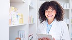 Happy chemist smiling and laughing while working in a drugstore and using a tablet. Young female pharmacist packing prescription medicine and prescription medication on shelves in the pharmacy