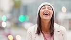 Portrait of laughing girl with bokeh lights in winter looking joyful. Cute and happy young woman smiling, enjoying a walk outside on a cold day in the city isolated against a blurred urban background