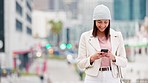 Trendy casual woman using her phone outside in an urban city. Young happy girl searching for her location during her commute in a modern town. Cheerful brunette texting online while waiting outside