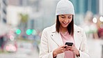 A woman laughing while reading a funny text on her phone on a cold day in an urban city. Trendy and cheerful female sending a message or using a mobile app to book a cab or taxi while traveling