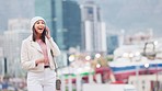 Trendy woman answering her phone while walking outside on a city street. Cheerful female talking and having a conversation on her mobile while traveling against an urban background on a cold day  