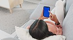 Woman streaming on blue screen phone, watching movies on subscription channel while choosing selection. Relaxed woman lying on home living room sofa, browsing social media and scrolling on dating app