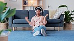 Woman listening to music and enjoying songs on wireless headphones, sitting on the living room floor inside. Young trendy african female with afro relaxing to her favorite podcast and meditating