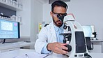 Male scientist looking through microscope and taking a closer look at a blood sample and writing notes on his findings in a medical research laboratory. Biotechnology specialist does analysis of dna