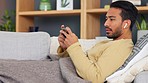 Asian man yawning while watching and streaming movies and series online on a phone while relaxing on the couch alone at home. Tired young male feeling sleepy while playing games on the web on sofa