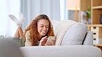 Young woman smiling and laughing while texting on a phone at home. Cheerful female chatting to her friends on social media, browsing online and watching funny internet memes while relaxing on a sofa