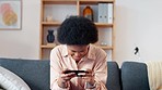 Playful woman playing games on her phone, sitting and relaxing on a couch at home. Young stylish female enjoying some online entertainment using a mobile device on a sofa in her house