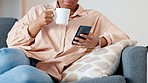 Woman reading a phone with funny memes on social media, drinking coffee and relaxing on sofa. Closeup of happy black female catching up with latest trends while browsing the internet and chatting