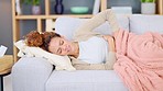 Sick Female needing medicine for period cramps or discomfort from an upset tummy.  Caucasian young lady in pain rubbing her stomach while lying alone under a blanket on the sofa at home. 