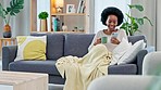 Happy woman reading social media news on a phone while drinking coffee on a sofa at home. Young African American female texting and sharing interesting funny and humorous content on the internet