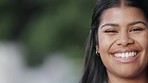 Close up portrait of a young woman smiling and looking cheerful while standing against a blurred background alone. The face of one happy and joyful young female laughing while feeling confident