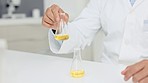 Closeup hands of a scientist conducting an experiment with yellow liquid in a research laboratory. Researcher mixing sample in beakers in a chemical or science lab. Doing an experiment to find a cure