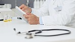 Closeup of male doctor's hands using digital tablet. Medical expert scrolling and zooming on high tech device. Sitting and checking results in lab with stethoscope on desk and equipment in background