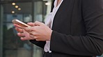 Hands of a person texting and browsing online on a phone while standing in an office alone at work. Corporate business professional searching internet and scrolling through social media on a break