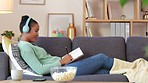 Black student streaming an audio book while making notes in a diary and relaxing on a couch. Young African American making a list of creative ideas while enjoying an online podcast in a living room