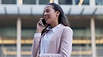 Business woman on the go, answering a phone call in against an urban background. Young female smiling while travelling for work  in a city. Professional woman discussing plans with a client 