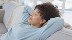 African american woman taking a deep breath and relaxing on her living room sofa at home. A young woman resting on a comfortable couch in the lounge and enjoying her off day alone on the weekend.

