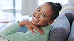 Portrait of a cheerful black woman relaxing on a couch at home, enjoying some quiet time alone on the weekend. Young carefree African American female laughing while sitting in a living room 