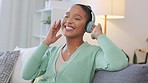 Woman listening to music on headphones, dancing and feeling expressive with increased serotonin in a home living room. Carefree, fun and smiling woman enjoying loud audio songs while relaxing on sofa