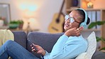 Woman streaming music on phone while wearing headphones and singing along while relaxing at home. Cheerful african female on couch listening to her favorite songs on a mobile app over the weekend 
