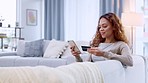 Credit card holder making online purchase on her phone on a sofa. Happy woman applying for a loan via a digital banking app. Female paying off insurance debt with modern tech and feeling satisfied