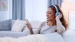 Woman listening to music from phone on headphones, enjoying and nodding her head with increased serotonin in home living room. Relaxed woman browsing song playlist on technology and relaxing on sofa